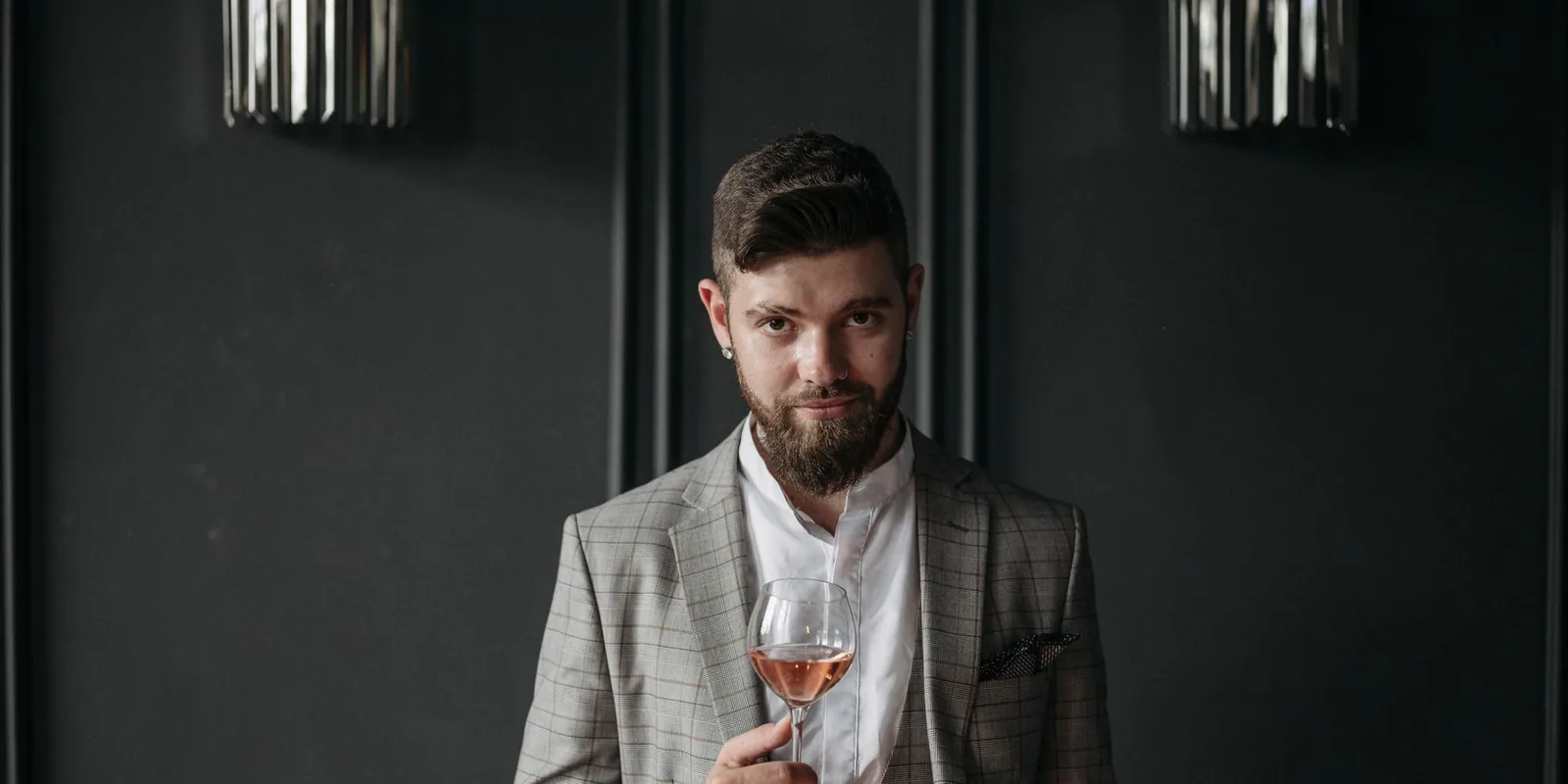 Bearded man in a gray blazer enjoying a glass of wine indoors. Elegant and sophisticated ambiance