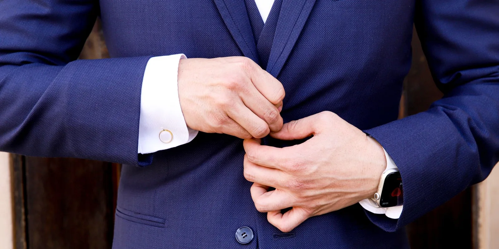 Close-up of a man's hands fastening a navy suit button, showcasing elegance and style