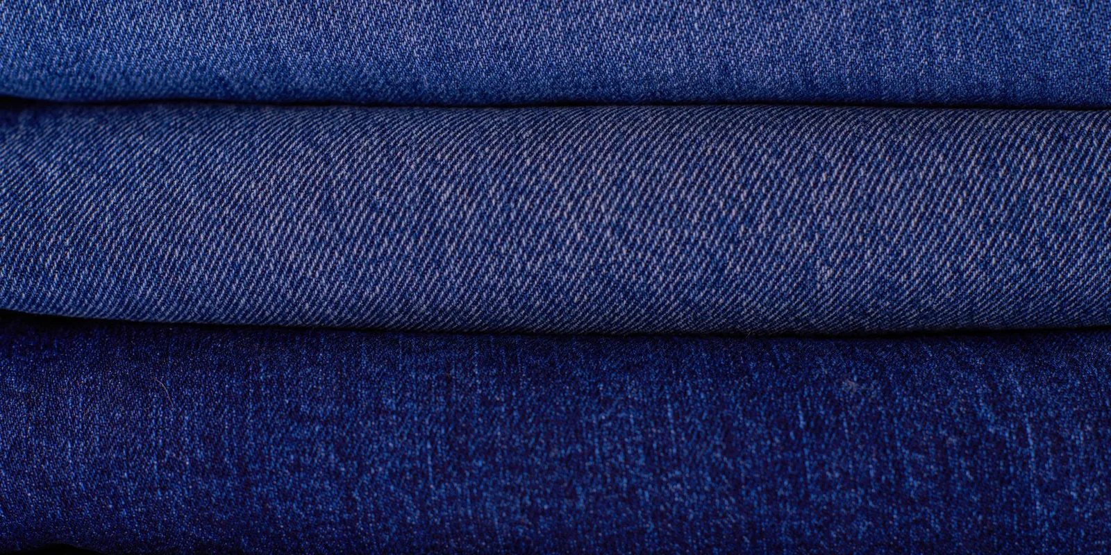 Close-up of neatly stacked folded denim fabrics in varying blue tones showcasing texture and pattern
