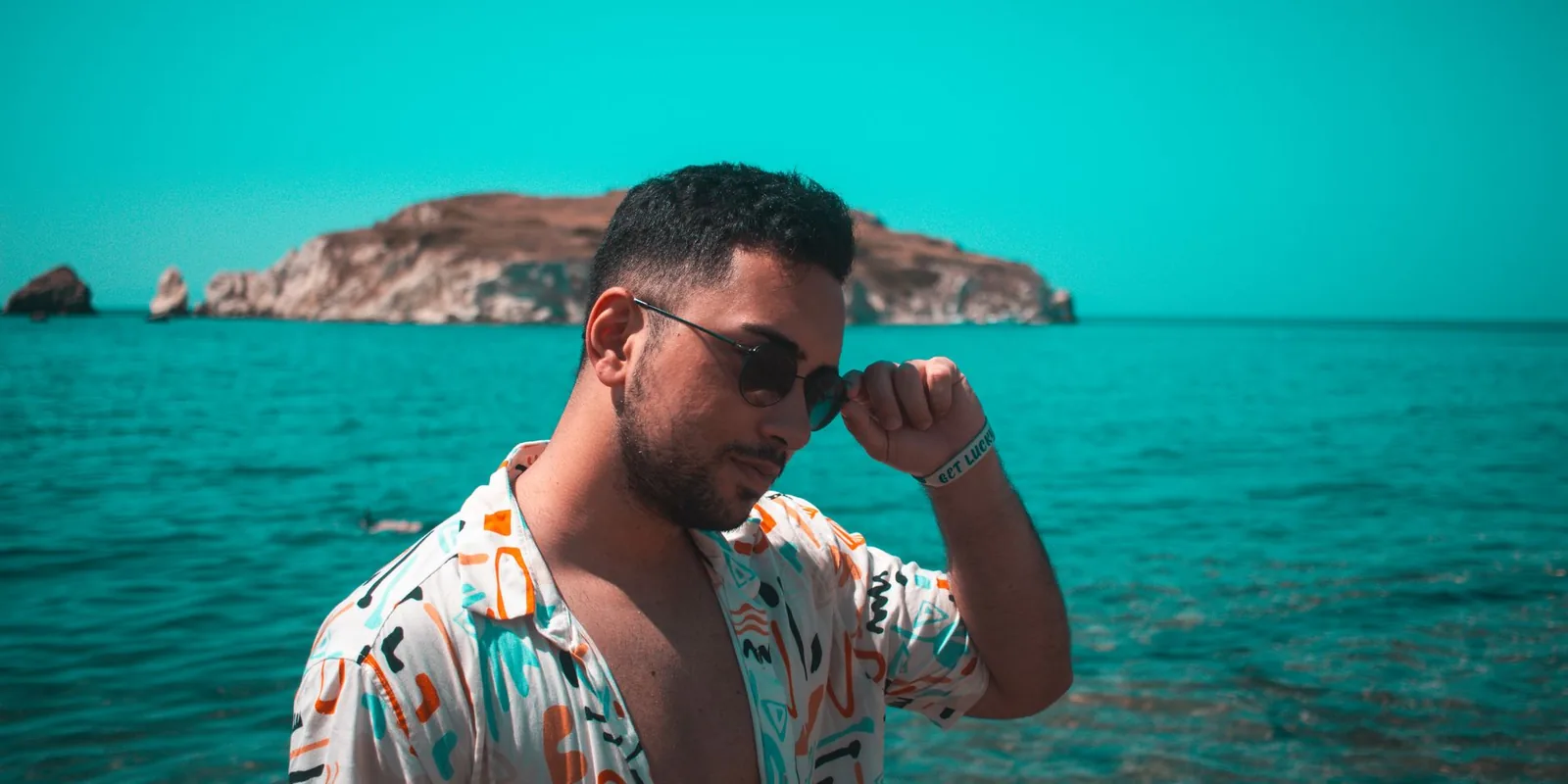 A fashionable man in sunglasses posing by the sea with scenic background