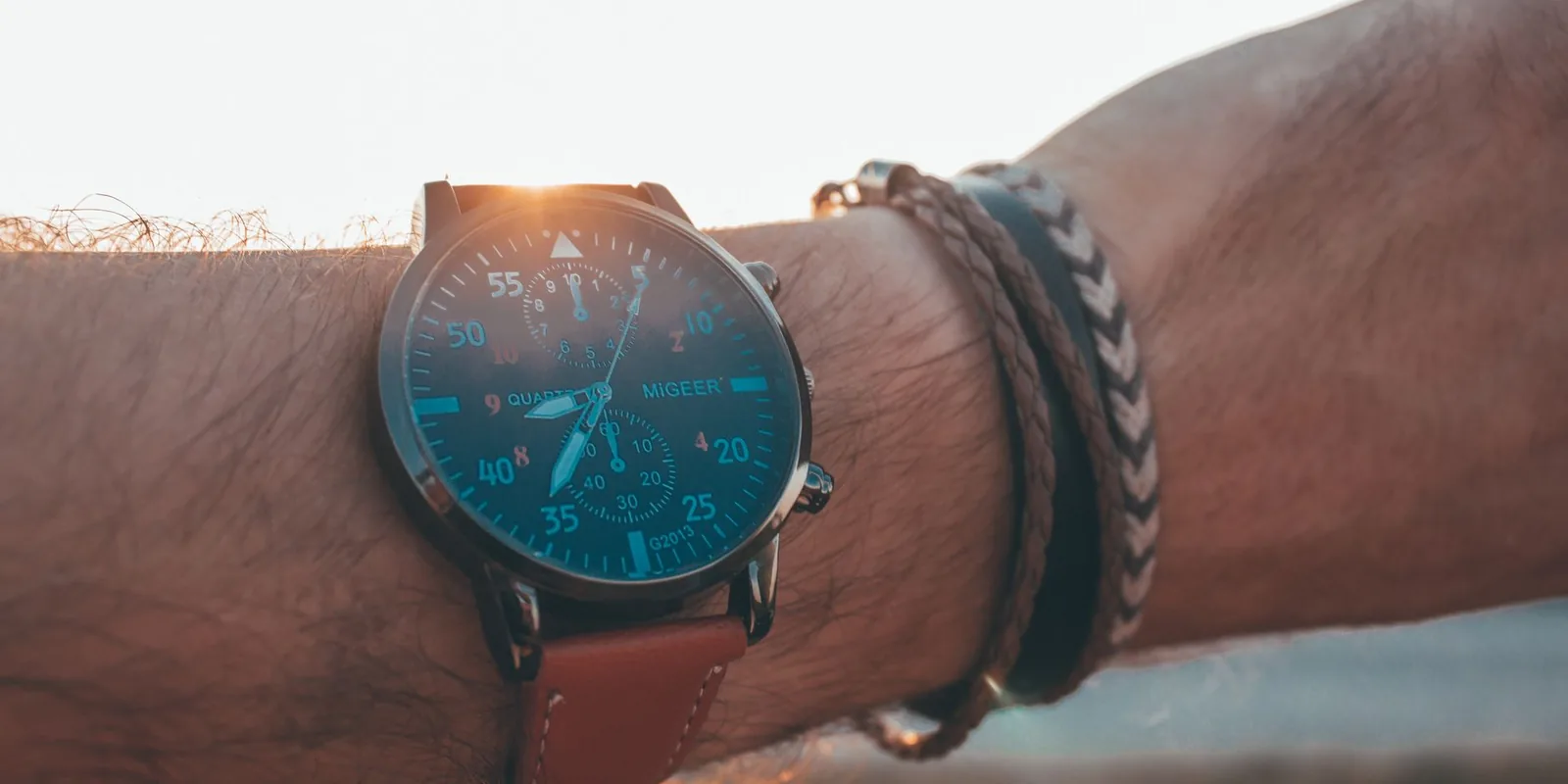 Close-up of a wristwatch and bracelets on wrist against a sunset backdrop