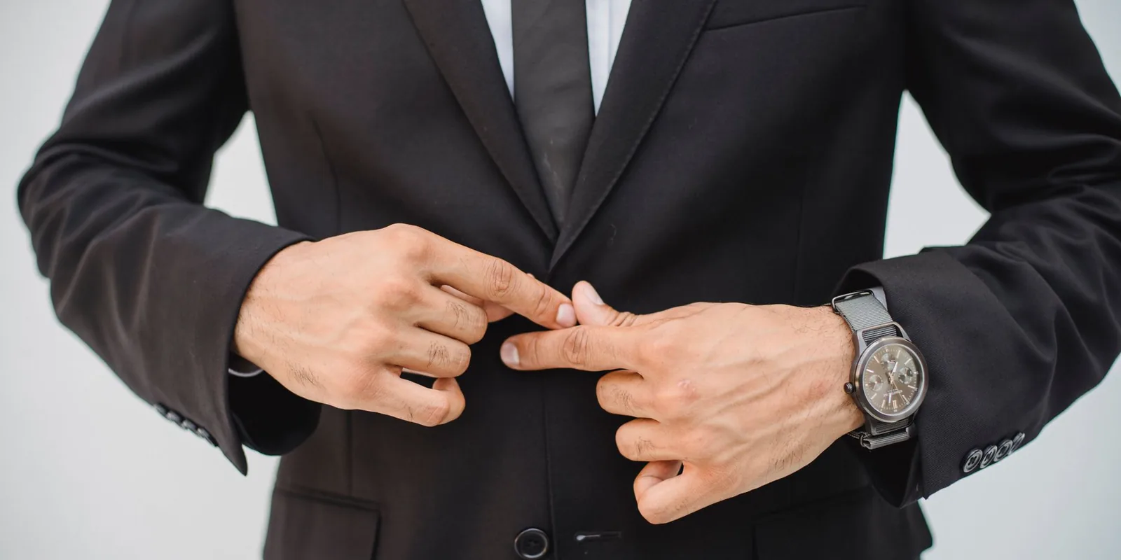 Close-up of a man's hands adjusting a black suit jacket, showcasing confidence and style