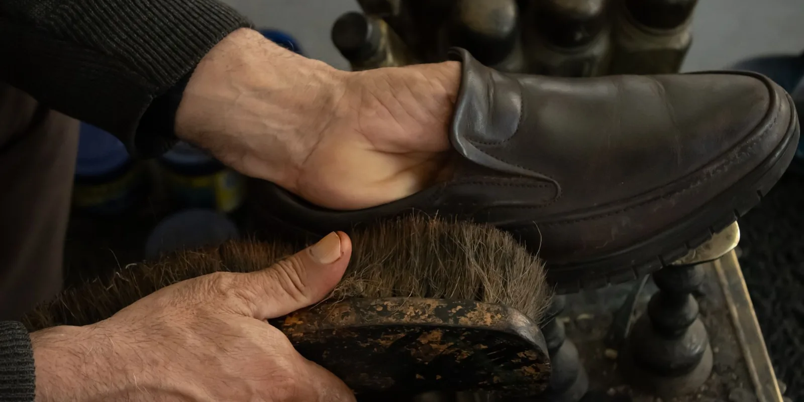 Detailed view of a shoe being polished by hand using a brush in a workshop setting