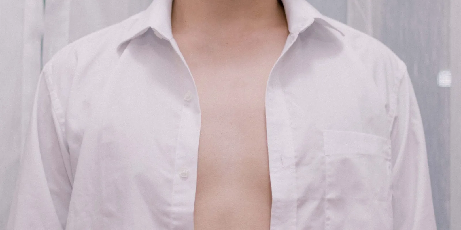 Close-up of a person wearing an unzipped white shirt on a neutral background, highlighting casual fashion style