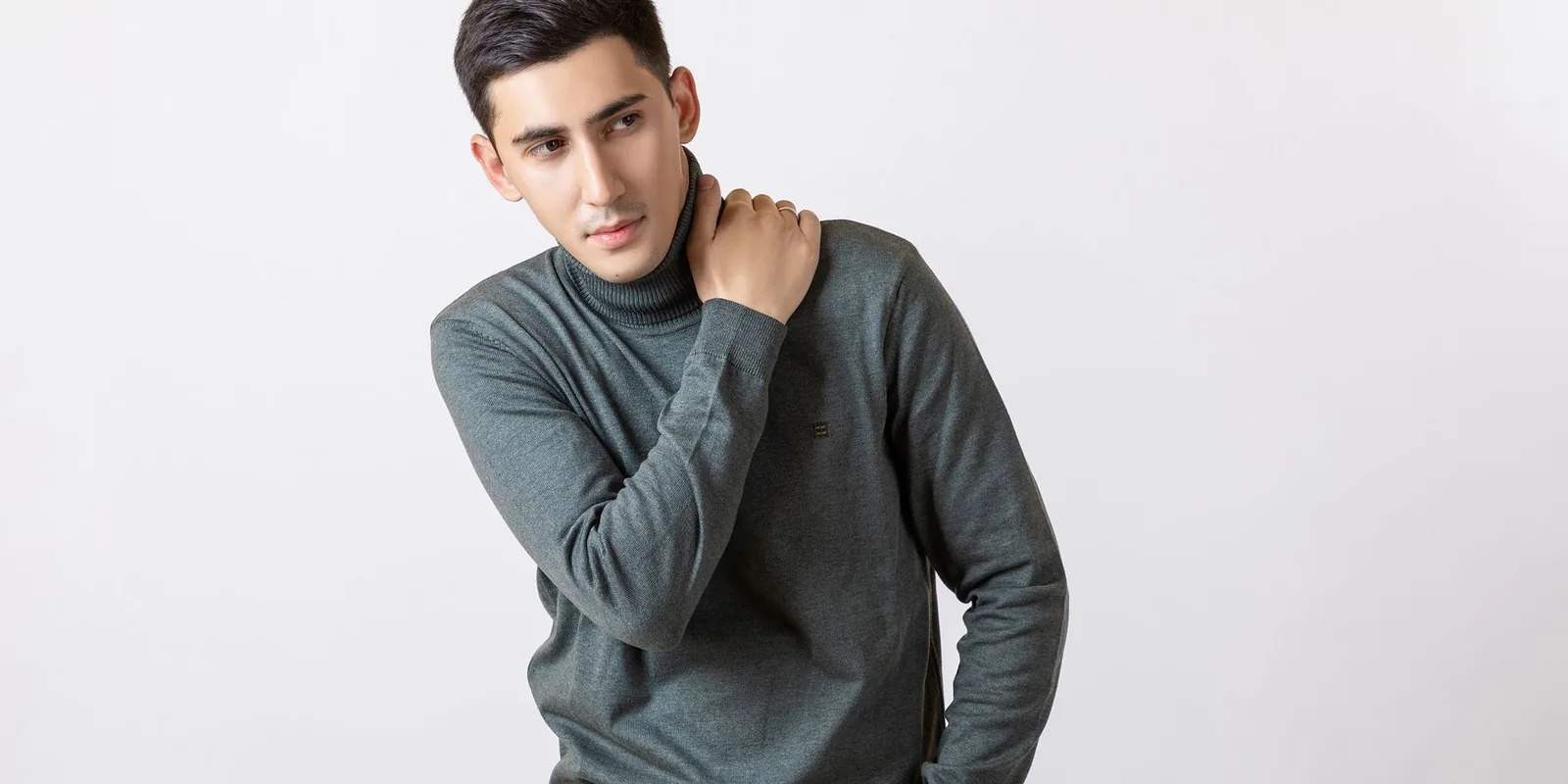 Young man in a gray turtleneck sweater posing in a studio setting