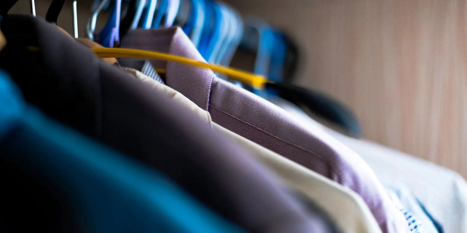 Close-up of various shirts hanging on colorful hangers inside a wardrobe