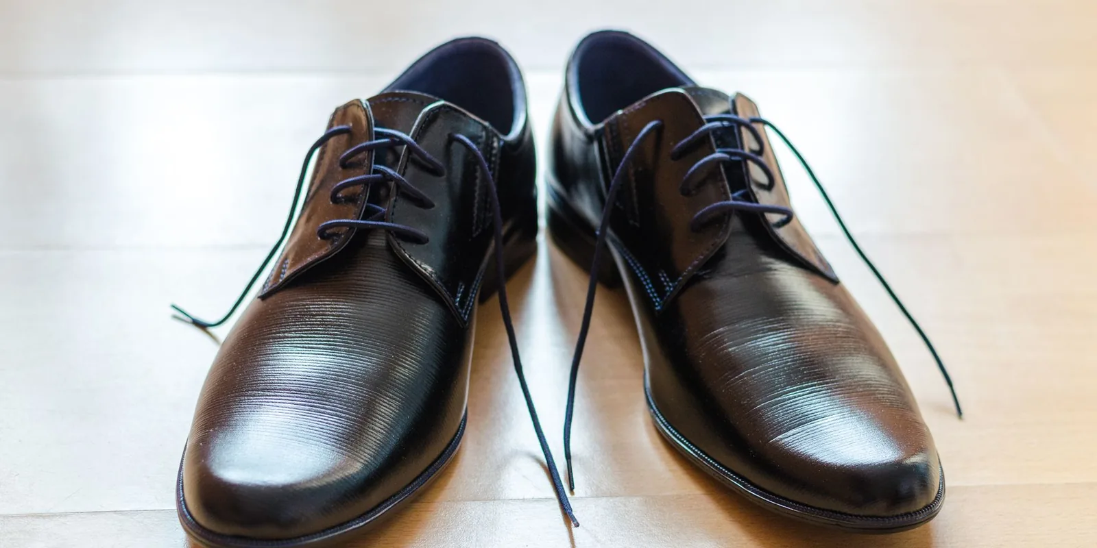 A pair of shiny, elegant black leather dress shoes with laces on a wooden floor