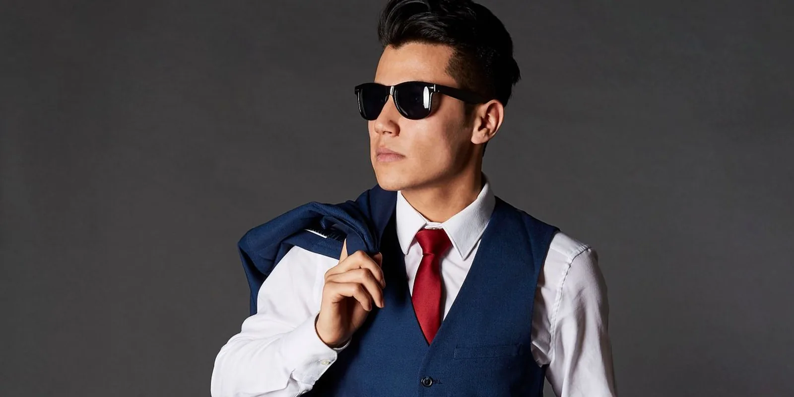 Portrait of a stylish man in a blue suit and sunglasses posing confidently indoors