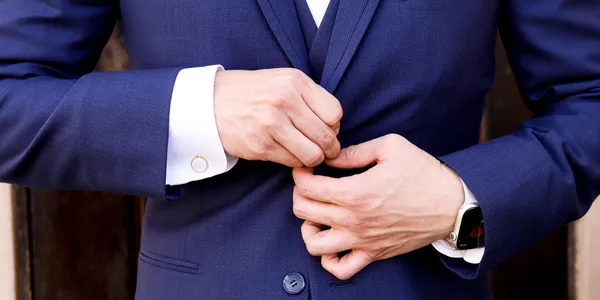 Close-up of a man's hands fastening a navy suit button, showcasing elegance and style