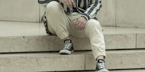 Man in striped shirt and sneakers sits on marble steps, showcasing casual fashion