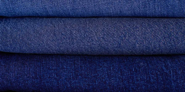 Close-up of neatly stacked folded denim fabrics in varying blue tones showcasing texture and pattern