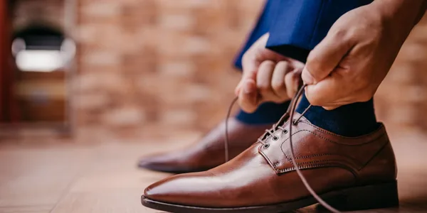 Close-up of a man tying laces on elegant brown leather shoes indoors