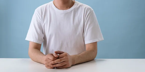 Close-up image of a person in a white T-shirt sitting at a white table against a blue background
