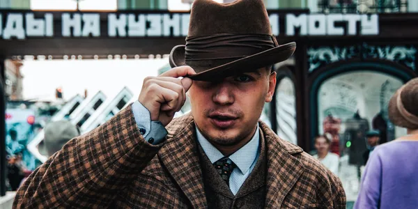 Portrait of a stylish man in a brown plaid coat and fedora, captured with selective focus on a city street
