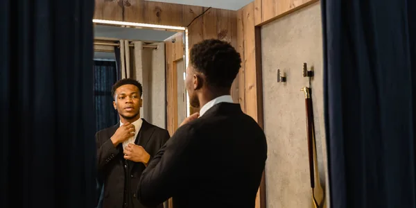 Stylish man adjusts his tie in a fitting room mirror, reflecting business confidence