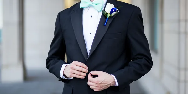 Sophisticated groom in a black tuxedo buttoning his jacket, adorned with a fresh boutonniere