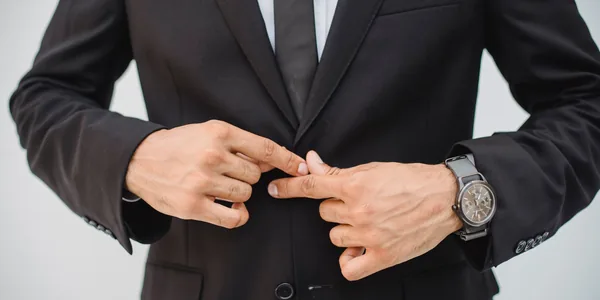 Close-up of a man's hands adjusting a black suit jacket, showcasing confidence and style
