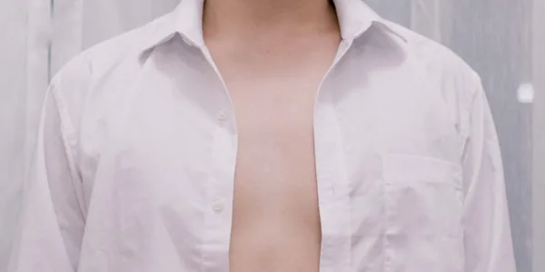 Close-up of a person wearing an unzipped white shirt on a neutral background, highlighting casual fashion style
