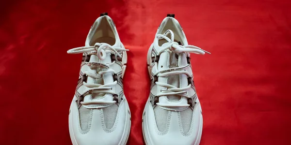 Top view of fashionable white sneakers on a bold red background, perfect for footwear fashion and design
