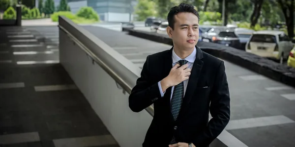 Confident young man in a suit adjusts his tie outdoors, exuding professionalism