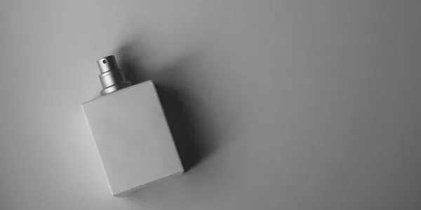 A sleek white perfume bottle photographed on a gray background with soft, muted lighting