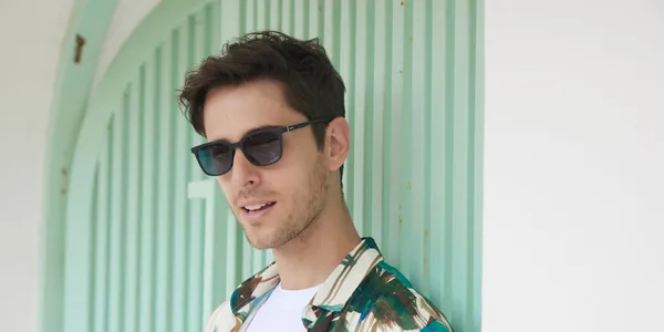 Young man in sunglasses posing against a mint green wall, showcasing summer fashion style