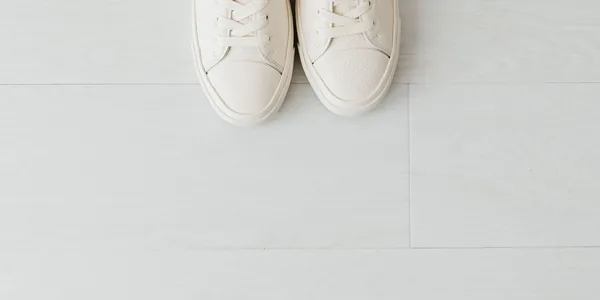 Close-up of white sneakers on a light wood floor with empty space