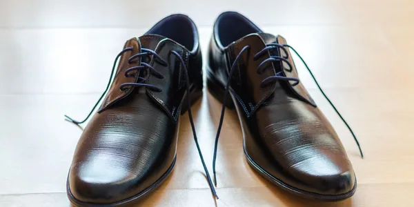 A pair of shiny, elegant black leather dress shoes with laces on a wooden floor