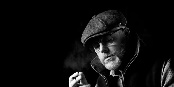 Stylish black and white portrait of a man in a flat cap smoking, captured in dramatic lighting