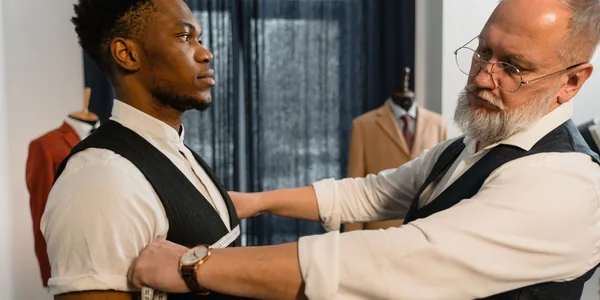 Professional tailor takes measurements for a bespoke suit fitting in a tailoring workshop