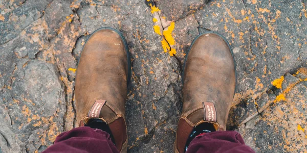 Close-up of brown leather boots standing on a textured stone path, showcasing rugged style