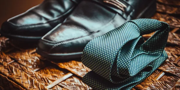 Close-up of a stylish necktie and polished leather shoes resting on a woven wicker surface