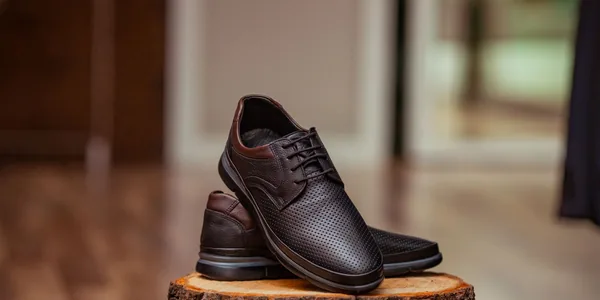 Stylish perforated leather shoes displayed elegantly on a rustic wooden stump indoors