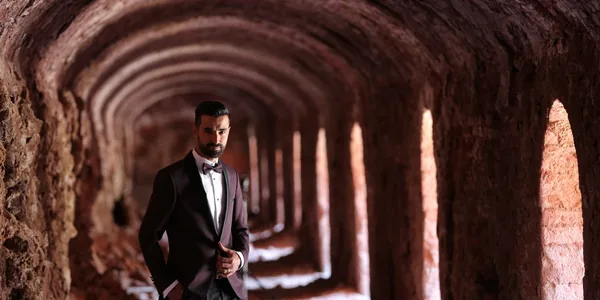 Fashionable man in a black suit posing in a brick tunnel, exuding confidence and style