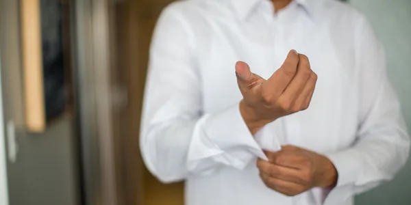 Close-up of a man adjusting his shirt cuffs, focusing on a white long-sleeve shirt indoors