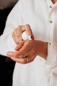 person squirting white body lotion onto wrist