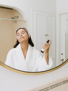 woman in white bathrobe holding body spray