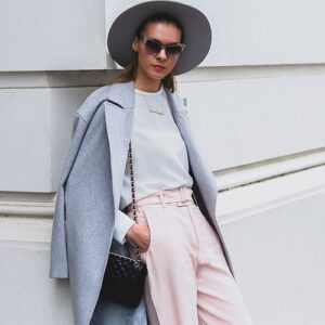 a lady wearing a hat and sunglasses leaning back against a wall